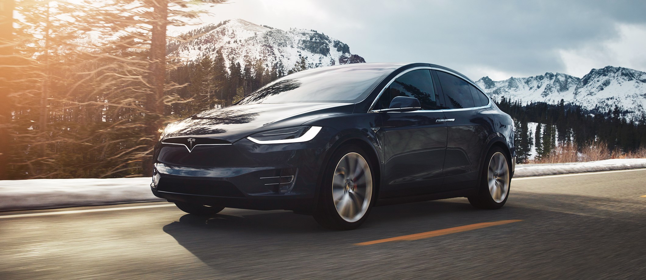 Black Tesla Model X driving with snowy mountains background